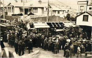 Tram accident on the corner of Pirie and Brougham Streets, Mount Victoria, showing crowds surrounding the scene and a police van at left. Photograph taken January 1920 by an unknown photographer. National Library of New Zealand PAColl-D-0927-2 
